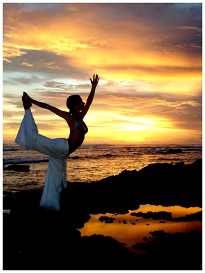 woman doing hatha yoga on sea beach under colorful sky