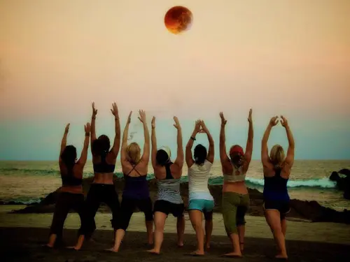 group of women doing hatha yoga on beach